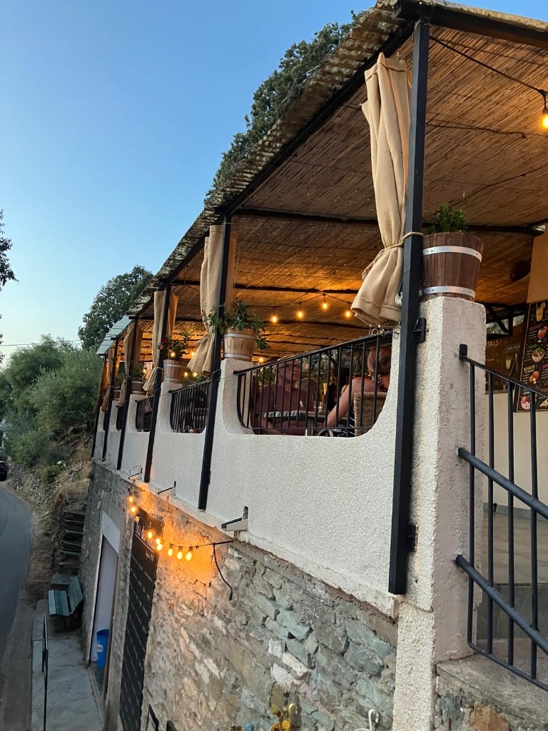 La terrasse du Bar des Amis en pierre, guirlandes et cannisse au crépuscule